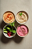Top view of bowls with assorted hummus served on table with fresh cucumbers and radish