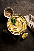 Top view bowl of delicious homemade hummus served on table with slice of lemon and chopped nuts