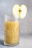 Fresh apple smoothie served in glass with sliced apple on concrete background