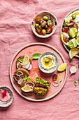 Top view of plate with delicious cream cheese and assorted vegetables placed on napkin near vegan fritters on pink background