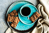From above ceramic plate with fresh baked chocolate cookies near black coffee drink in a mug on concrete background