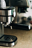 Moderne Kaffeemaschine aus Edelstahl mit Manometer auf einem Tisch in einem Haus mit unscharfem Hintergrund