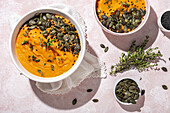 From above of white ceramic bowls with delicious healthy pumpkin cream soup with seeds and rosemary placed on table in kitchen