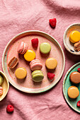 Top view of assorted round plates with various of sweet colorful French macaroons and berries on pink tablecloth