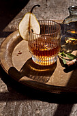 From above of elegant glass of cold whiskey decorated with pear slice served on tray with cigar in daylight