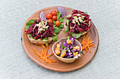 Hoher Winkel von leckeren Sandwiches mit Salat und Roter Bete, serviert mit Gemüse und frischem Salat in einer Schüssel auf einer Holzplatte auf einem Tisch