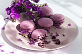 Bunch of delicious violet macaroons served on plate near delicate flowers on sunlit table