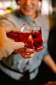 Soft focus of crop unrecognizable female barkeeper clinking with alcoholic red blood shots with faceless person while working in bar