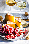 From above cheese variation with fresh fruits on the stone plate and white wine in the glass on the concrete table