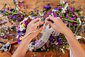 Crop anonymous female florist creating wreath from fresh colorful flowers while working at table in shop