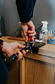 Crop faceless barista standing at table and preparing fresh aromatic coffee while working in cafeteria in daytime
