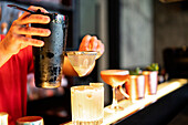 Focused cropped unrecognizable bartender pouring cold refreshing cocktail through strainer in glass placed on counter in bar