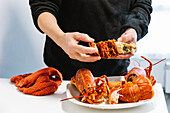 Crop anonymous person cracking tasty cooked red lobster with meat with hands on white table in light kitchen at home