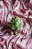 Top view of green artichoke with small beads on crumpled silk fabric
