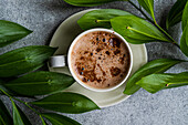 Cup of cappuccino and green leaves of Ruscus plant