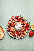 Top view of appetizing fresh strawberries and lemon served with burrata cheese on plate