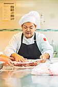 Female chef in uniform and apron covering raw meat with clingfilm while cooking in kitchen