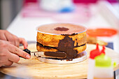 Crop unrecognizable person making biscuit cake with chocolate on wooden stand in bakery