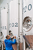 Back view of male engineer taking notes on paper on metal vessel in beer factory