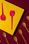 Overhead view of bright red and brown eco friendly spoons near yellow carton sheet