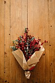 From above of festive stylish decorative Christmas bouquet with twigs of eucalyptus and bright red branches with berries placed on wooden table in room