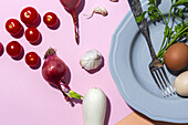 Hühnereier von oben auf einem Teller mit Gabel vor frischen Petersilienzweigen und Kirschtomaten auf zweifarbigem Hintergrund