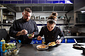 Male and female chefs arranging ingredients on bowl while preparing tasty dish in contemporary restaurant kitchen together