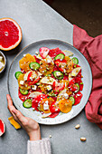 Overhead of crop person eating delicious healthy salad with strawberry and orange and cucumber slices with cheese and pistachios on plate