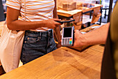 Cropped anonymous woman with fabric bag using smartphone to pay for groceries to vendor while visiting zero waste shop