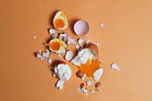 Top view of soft boiled chicken eggs and eggshell scattered on peach background in studio