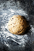 Top view of pile of kneaded dough with raisins placed on flour dusted table