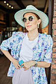 Smiling young female in stylish apparel with cellphone in cafeteria with lamps