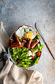 Gesundes Mittagessen mit frischem Bio-Gemüsesalat, Spiegelei und Würstchen, serviert auf einem Betontisch