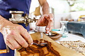 Selective focus of faceless anonymous bartender collecting coffee powder with spoon from wooden board into portafilter after grinding
