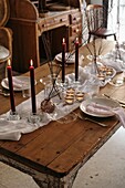 White tablecloth and plates placed on festive table decorated with burning candles and dry branches of tree