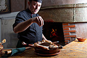 Crop focused male chef sprinkling salt on raw poultry in bowl while standing at table while preparing delicious dish in restaurant