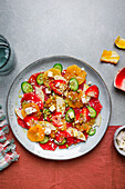 Blick von oben auf einen gesunden Salat mit Orangen, Erdbeeren, Äpfeln und Gurken, serviert mit Käse und Nüssen auf einem Teller