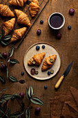 Von oben schmackhafte frisch gebackene Croissants auf einem Teller mit Früchten neben einer Tasse Tee auf einem Holztisch am Morgen in einem hellen Raum