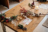 From above Christmas composition with colorful postcard with inscription Feliz Navidad placed near burning candles and cups of tea on wooden table decorated with colorful branches of plants