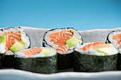 Close-up set of tasty Futomaki Norwegian sushi rolls with salmon and avocado served on blue background in light studio