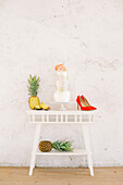 Fresh pineapples and tasty cake placed on table near red high heeled shoes against white wall during wedding celebration