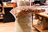 Soft focus of unrecognizable female vendor in striped apron carrying plastic bag of colorful fusilli pasta during work in grocery store