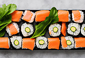 Appetitliche Sushi-Rollen mit Reis und Lachs, serviert auf einem Teller neben Salatblättern