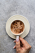 Top view of the ceramic cup of cappuccino with foam in the woman's hands