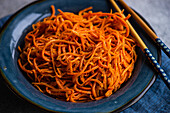 Traditioneller würziger asiatischer Karottensalat auf Keramikteller und Stäbchen auf einem Betonhintergrund