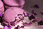 Köstliche violette Makronen auf einem Teller mit zarten Blumen auf einem Tisch im Sonnenlicht