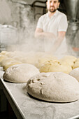 Crop ethnic male baker in uniform at table with raw bread dough and flour dust in bakery
