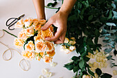 Anonymous adult Hispanic female florist with dark hair in apron arranging bouquet of assorted gentle fresh flowers against white background