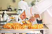 Crop anonymous chef in white uniform checking pastry with knife placed on tray during cooking process