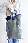Side view of crop anonymous female shopper carrying heavy reusable shopping bag with denim jeans